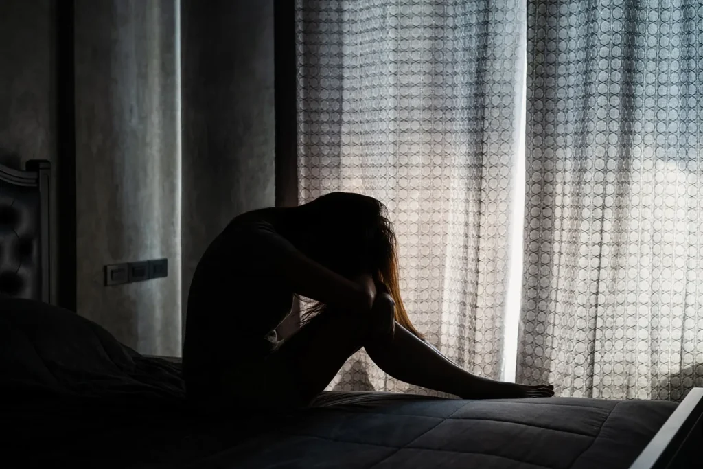 Silhouette of a distressed woman sitting on a bed with her head resting on her knees, representing protection and support from a Los Angeles restraining order lawyer.